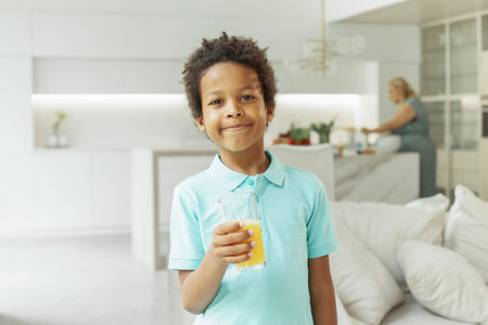 African American child boy drinking orange juice at homeの写真素材