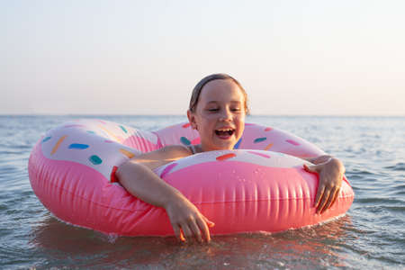 Happy little girl enjoying summer sea and floating on pink inflatable ring