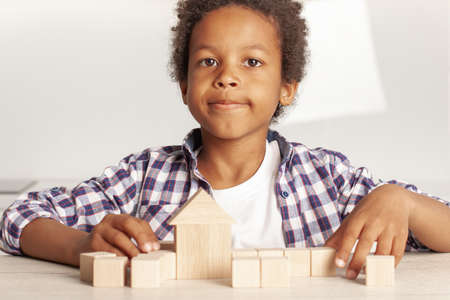 Happy cute little son kid playing game building constructor house from wooden blocks
