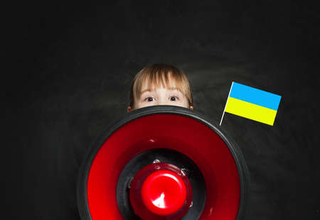Small kid with loudspeaker and Ukrainian flag on black background. No War in Ukraine conceptの写真素材