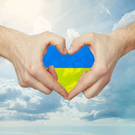Male hands making heart shape with Ukrainian flag against sky clouds backgroundの写真素材