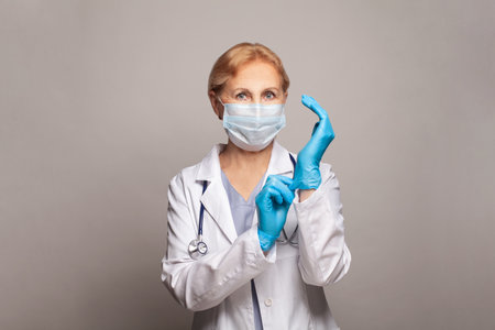 Portrait of an attractive senior female doctor in white coat and blue glovesの写真素材