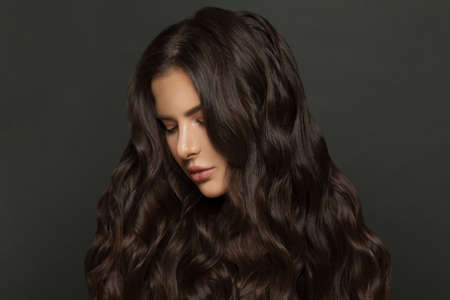 Perfect brunette woman with long and shiny wavy hair . Beautiful female model with curly hairstyle on black backgroundの写真素材