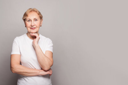 Beautiful senior lady smiling and looking at camera on white background. Mature woman 60s portrait