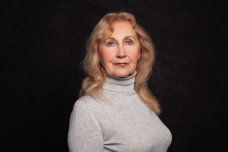 Blonde woman wearng gray turtleneck on black wall background