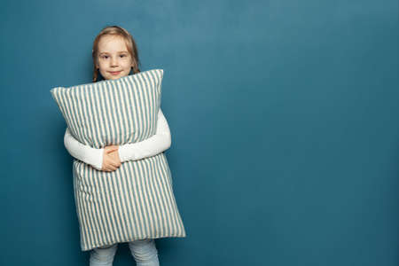 Cute young kid girl holding pillow on blue banner background with copy spaceの写真素材