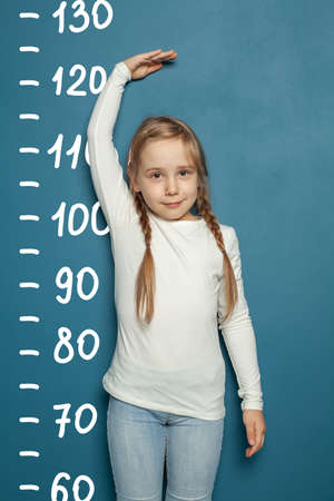 Cute little girl measuring height near blue wall background at homeの写真素材