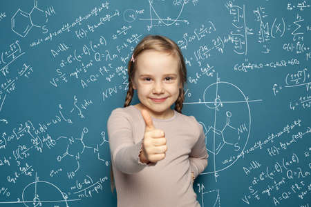 Happy smart kid girl smiling and holding thumb up on science formulas background