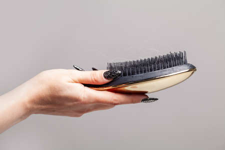 Black comb and hair in female hand, hair loss and hair care concept