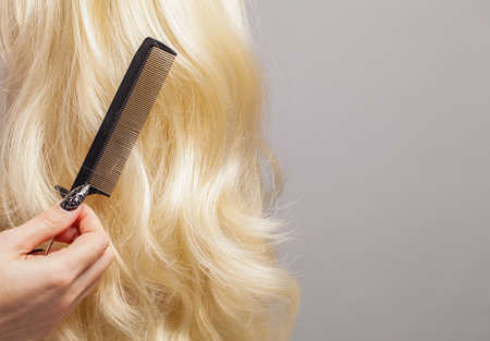 Hair care concept. Black comb and long curly blonde hair on gray studio background closeupの写真素材