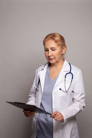 Mature woman doctor specialist in medical uniform thinking on gray background