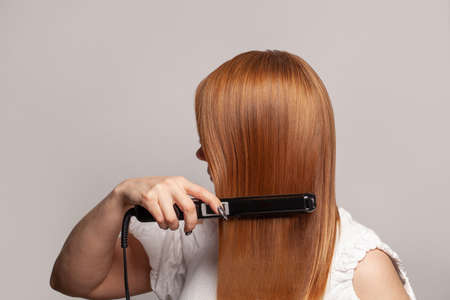 Redhead woman straightening hair with straightenerの写真素材