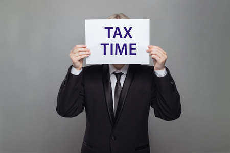 Businessman hiding her face  behind a time tax on white paper board on grey backgroundの写真素材
