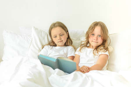 Little children reading book in bedroom at homeの写真素材