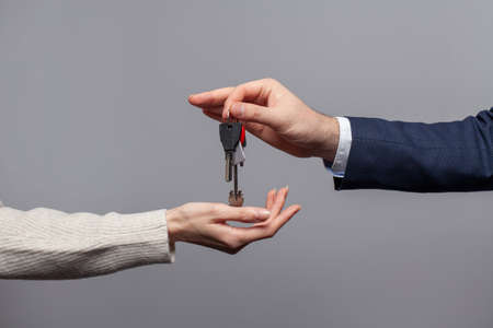 Male hand passing house keys to new owner on grey background