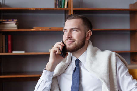 Happy young handsome businessman using phone indoor
