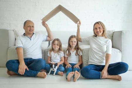 Smiling family parent with children with a symbol of roof indoor. Concept of housing for young...