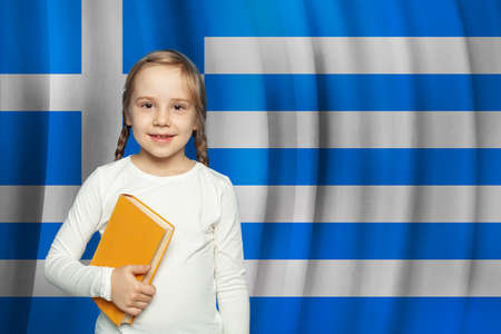 Cute Greek small girl child with book against flag of Greece backgroundの写真素材