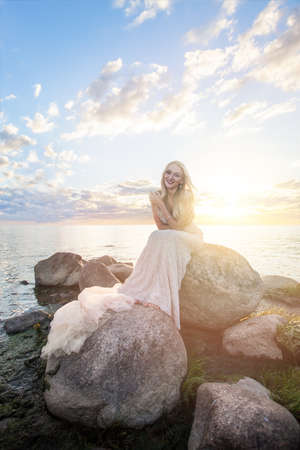 Smiling woman fashion model in evening gown outdoors, sunset lightの写真素材