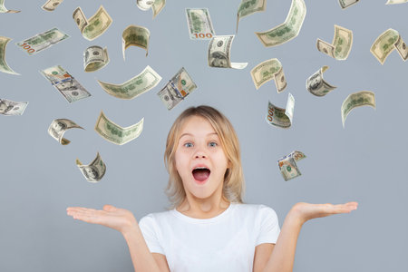Surprised teen girl with falling us dollar money on grey backgroundの写真素材