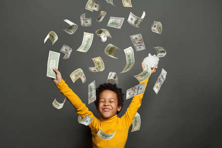 Happy little african american kid boy under us dollar money rain on black backgroundの写真素材