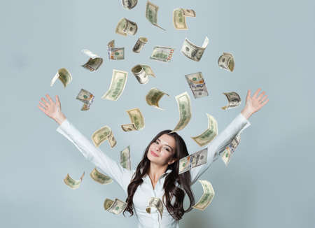 Happy smiling businesswoman with falling dollar cash money on grey backgroundの写真素材