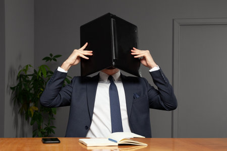 Frustrated stressed businessman hiding his head under laptop in officeの写真素材