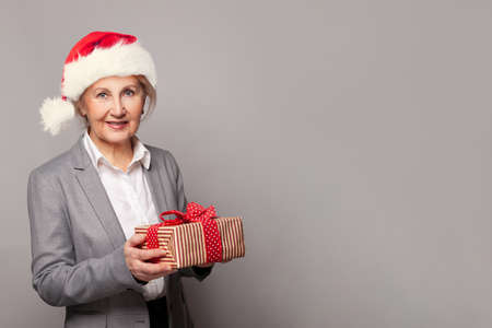 Beautiful lady in red Santa hat holding Christmas gift box and celebrating New Year, studio backgroundの写真素材