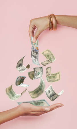 Hand giving cash us dollar money to other female hand on pastel pink backgroundの写真素材