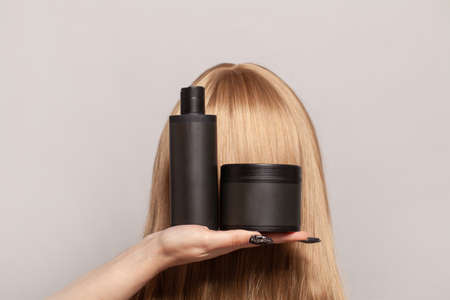 Plastic bottles of hair care and beauty products in female hand against blonde head.の写真素材