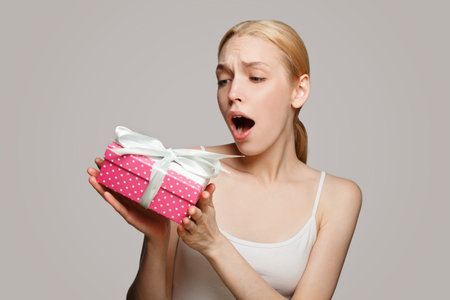 Surprised cute woman with pink gift with white ribbon on white backgroundの写真素材