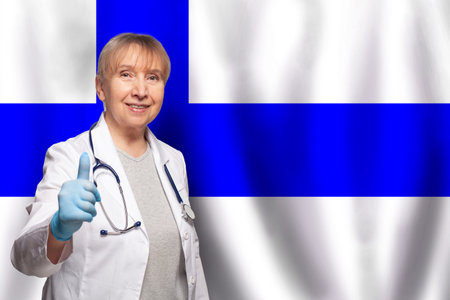 Finnish smiling mature doctor woman holding stethoscope on flag of Finland backgroundの写真素材