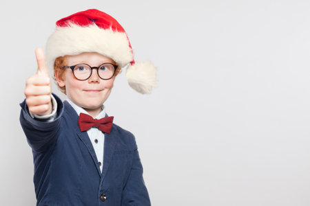 Cute child boy in Santa hat with thumb up on white backgroundの写真素材