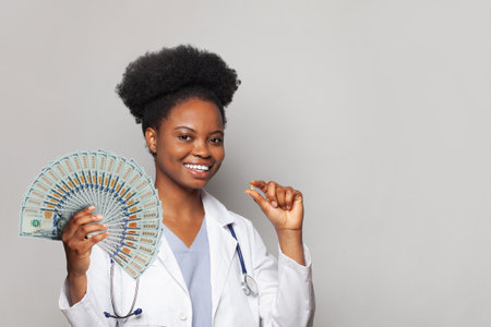 Nice successful african american woman doctor smiles and holds fan of money one hundred dollar against white backgroundの写真素材