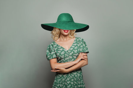 Happy woman with blonde curly hair wearing green dress and wide green hat and smilingの写真素材