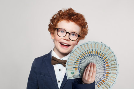 Happy child smart student boy in glasses and suit portrait with money us dollars fanの写真素材