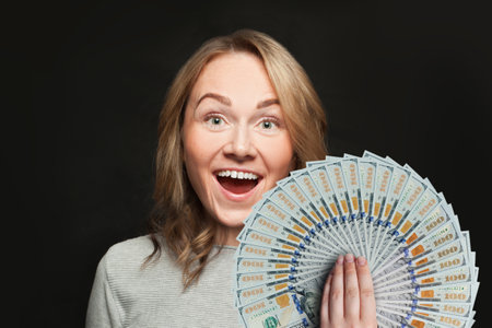 Surprised woman with open mouth and fan of money against black backgroundの写真素材