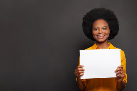 Smiling woman with white empty paper banner in her hand on black backgroundの写真素材