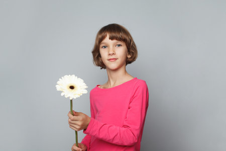 Little child girl in pink shirt holding white flower in her hands on white banner backgroundの写真素材