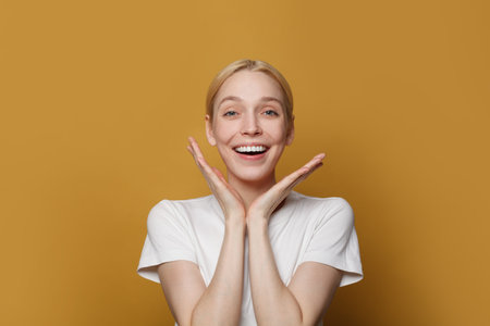 Portrait of happy attractive woman laughing and looking at camera against yellow studio wall background.の写真素材