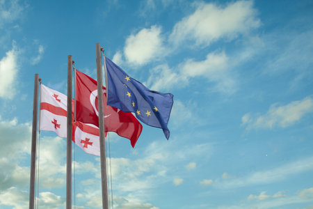 Georgian, Turkish and European Union flags on the background of blue cloudy sky