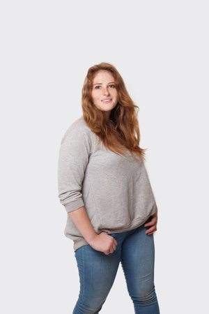 Happy positive curvy woman with long red hair standing on white backgroundの写真素材