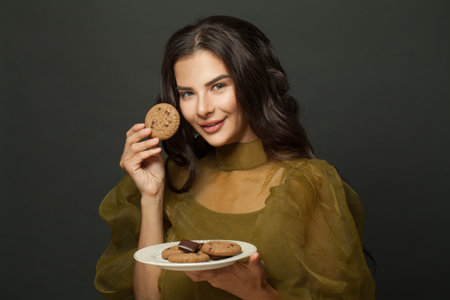 Happy cute woman eating cookies with chocolate chips on black backgroundの写真素材