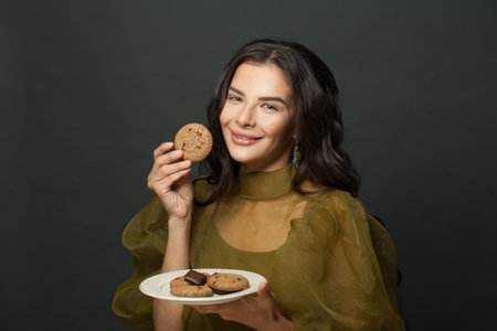 Lovely happy woman with cookies against black studio wall backgroundの写真素材