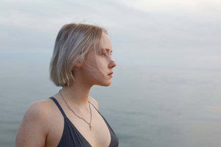 Portrait of young woman teenager girl 17 years old standing on romantic background of beautiful blue sea and cloudy skyの写真素材