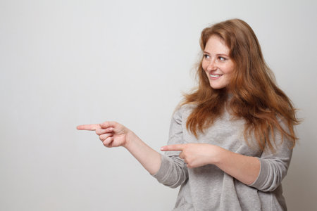 Young smiling woman pointing finger aside on white studio wall backgroundの写真素材