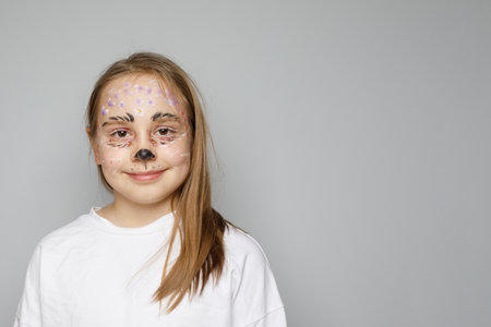 Cute funny child with paint on face smiling against gray studio wall background background. Helloween on birthday party with animators conceptの写真素材