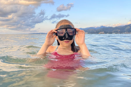 happy child girl in swimsuit and mask on sea at sunsetの写真素材