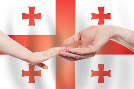 Georgian baby and parent hands on the background of flag of Georgia Help, aid, support, charity conceptの写真素材