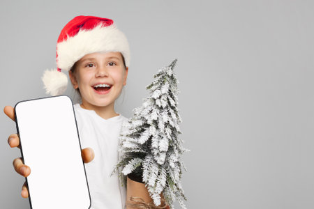Christmas child. Happy kid Santa with smartphone and green Xmas tree, Mockup bannerの写真素材